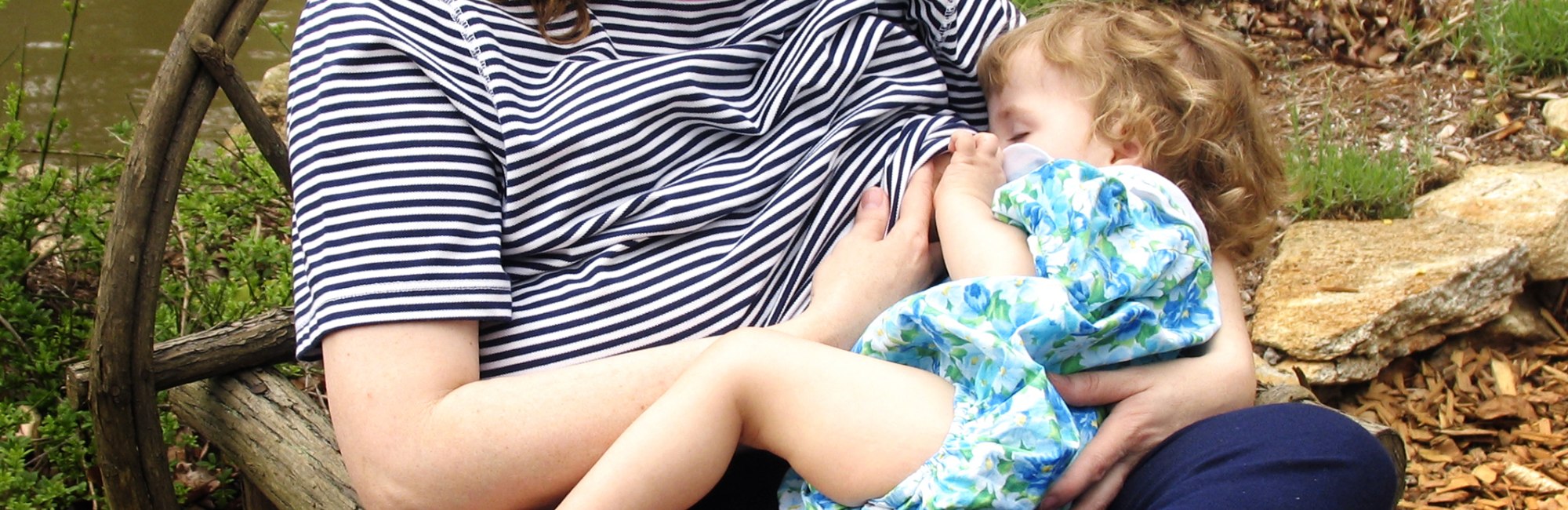 mother breastfeeds toddler outside in park