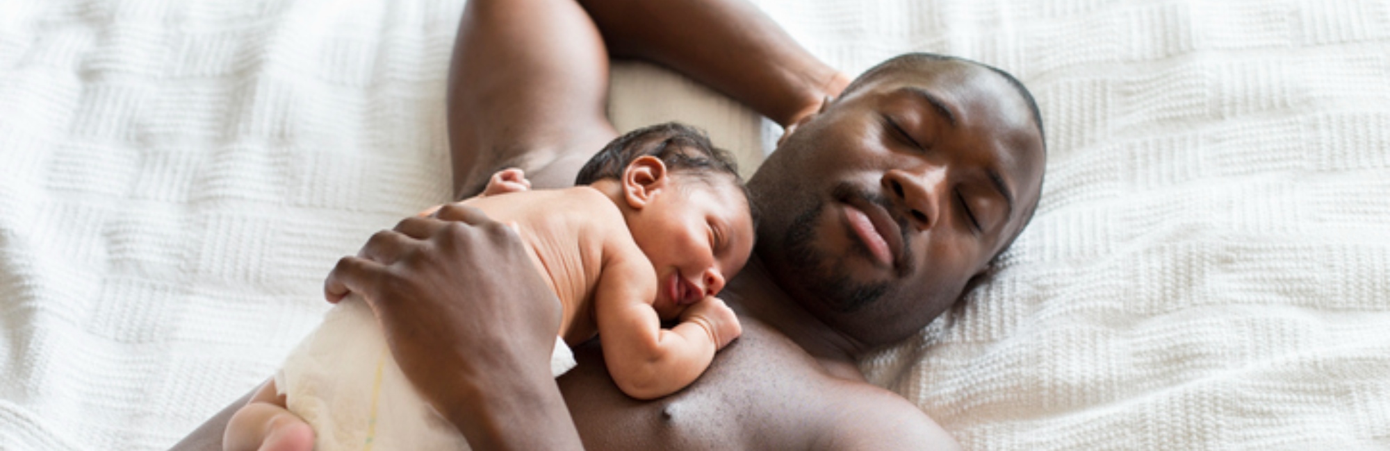 bare chested father lies down with sleeping baby on his chest