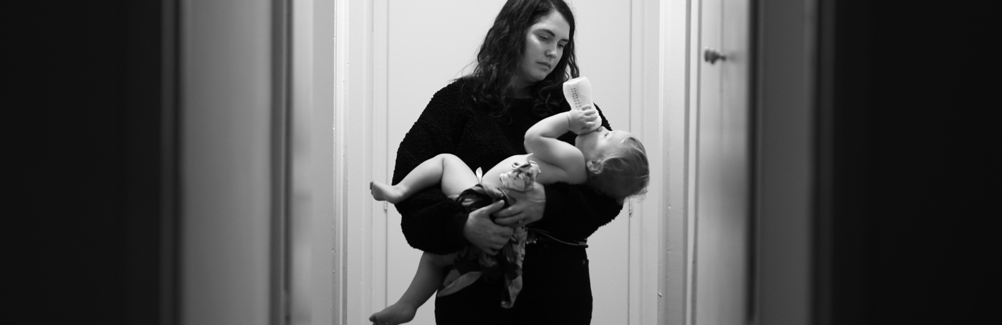 black and white photo of mother holding up toddler who is feeding themselves with a bottle