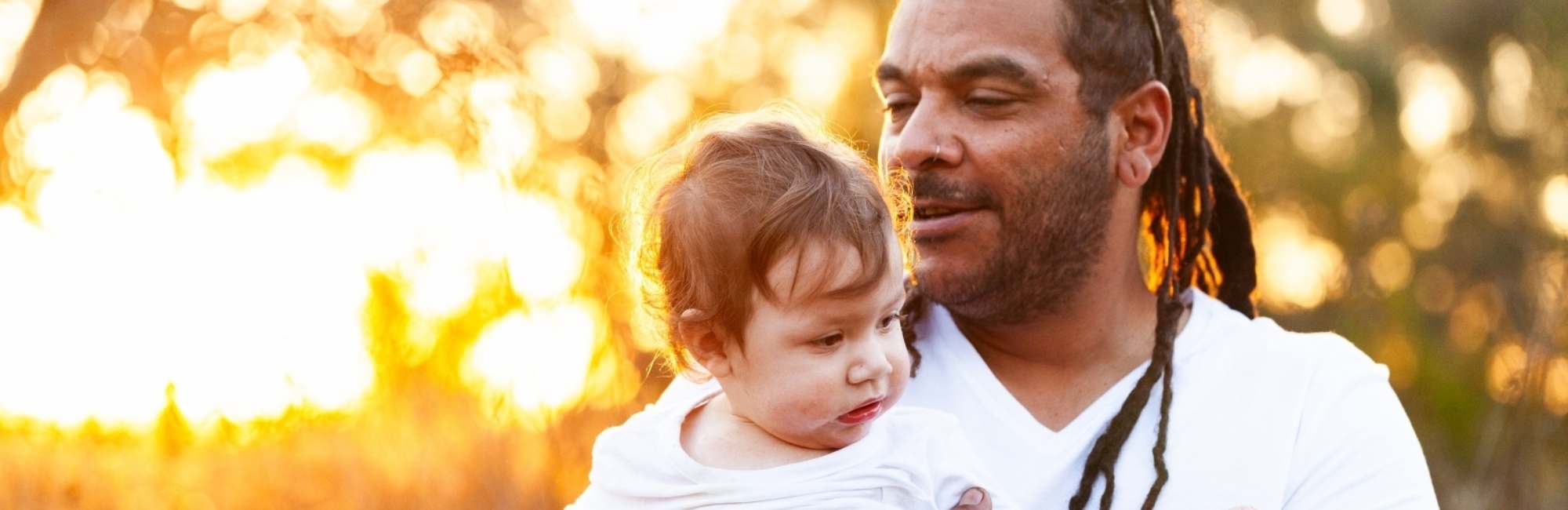 father with dreadlocks and nose piercing holds up toddler with allergies