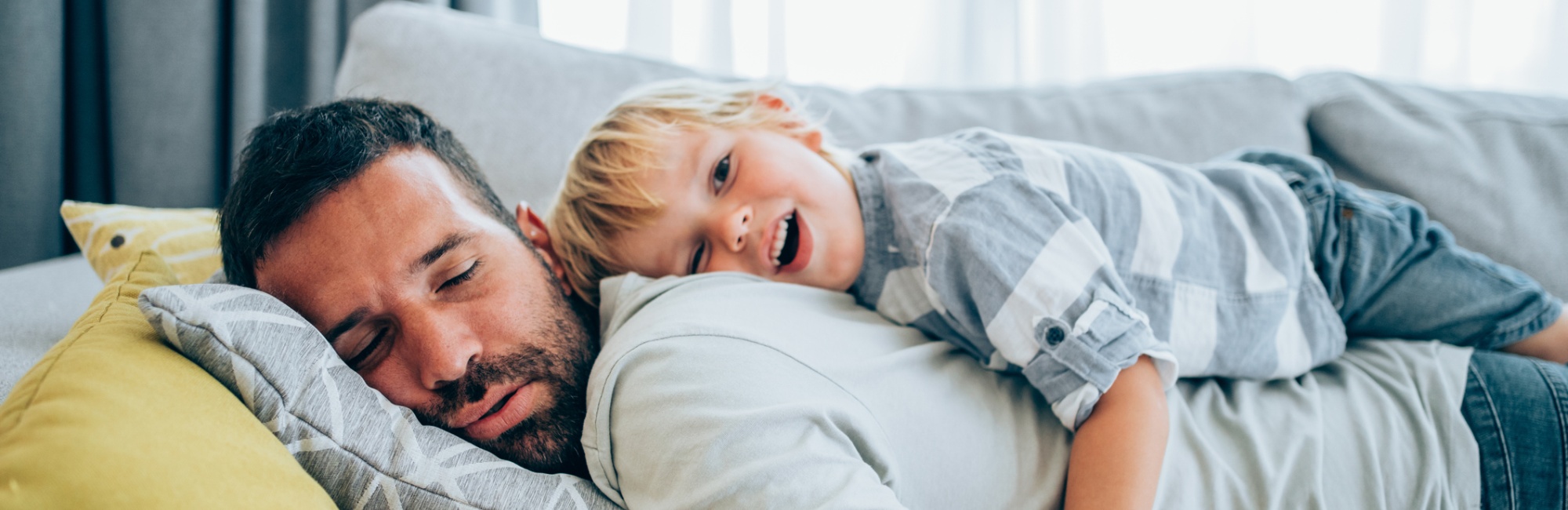 Sleeping father with chappy child laying on his back on couch