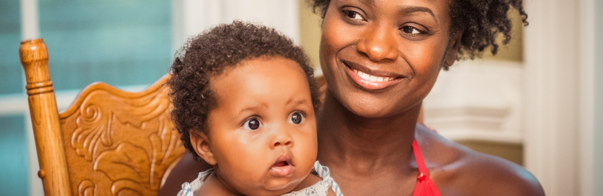 mother smiles as baby looks around while sitting on her lap