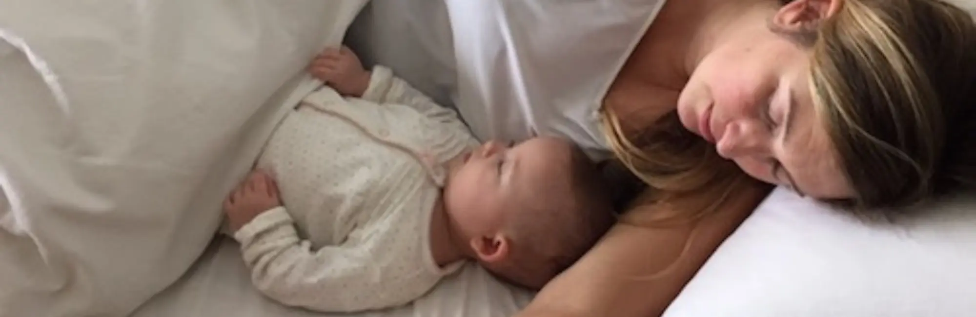 mother and baby in white clothing sleep together in bed