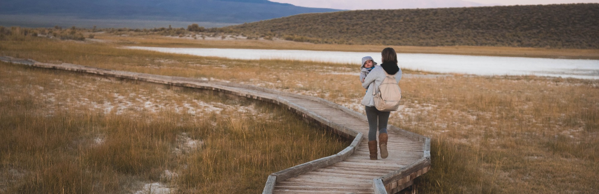 mother walking with child down boardwalk path through nature