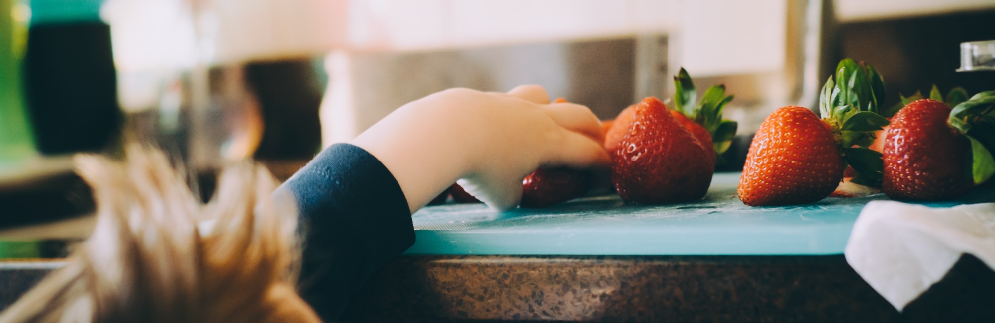 toddler reaches up to bench to grab a strawberry