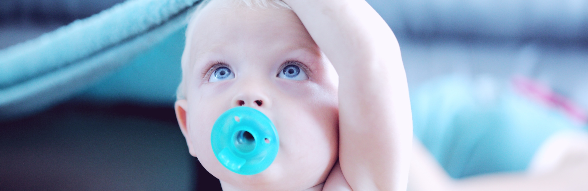 blue eyed caucasian baby using blue pacifier dummy