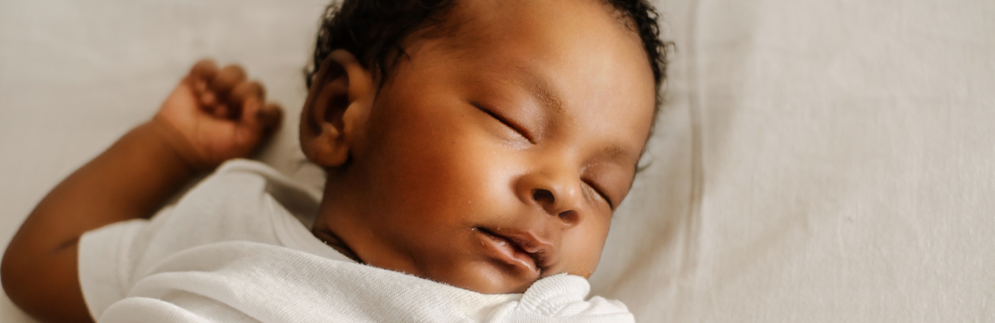 brown skinned baby with white clothing sleeps on back