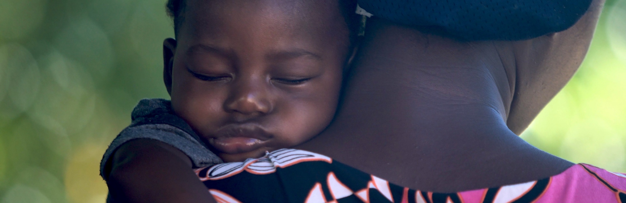Dark skinned baby sleeping over mother's shoulder